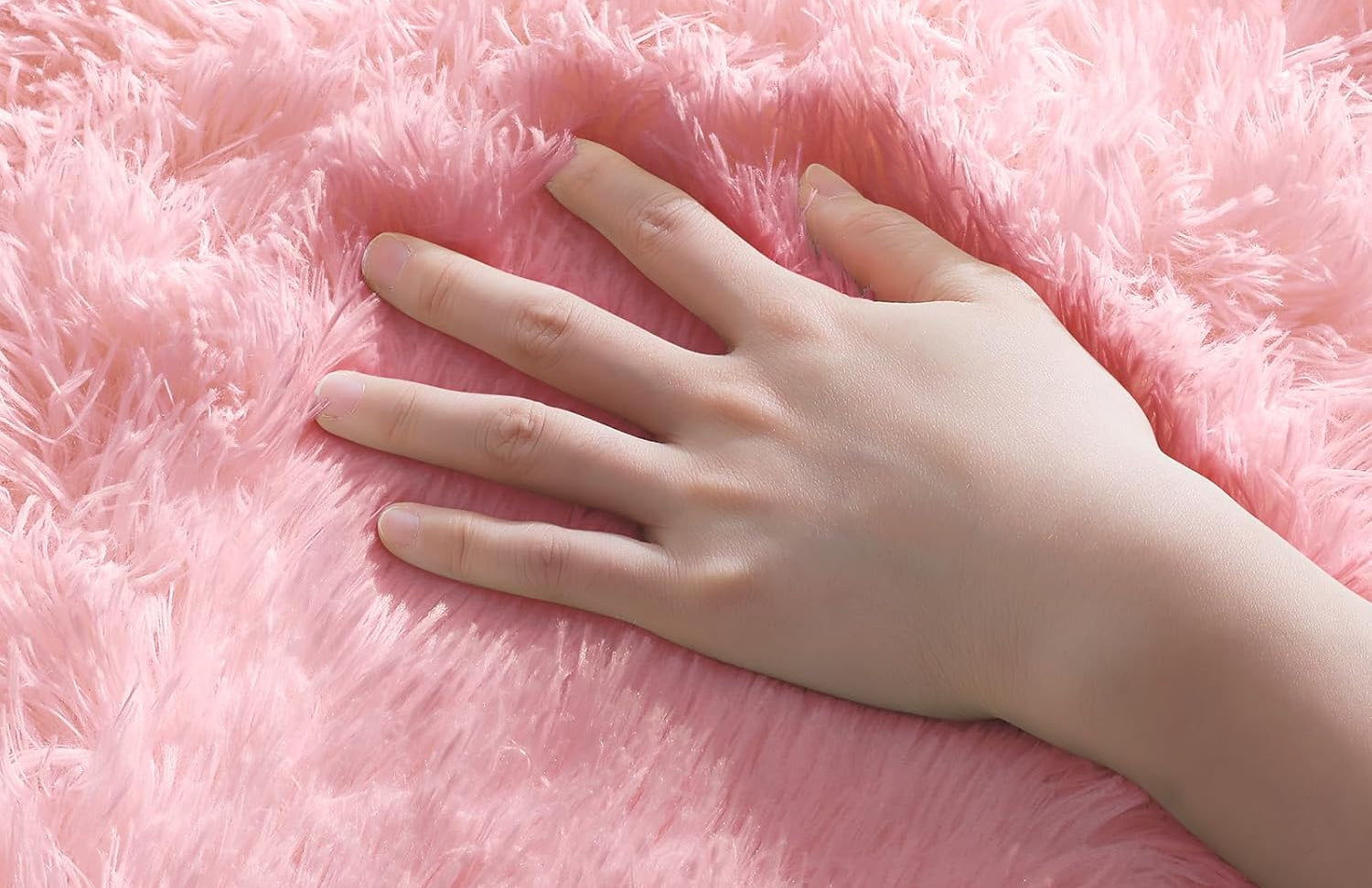 Pink fluffy rug with a hand touching it, highlighting the ultra-soft texture.